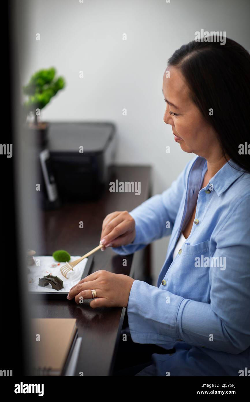 Businesswoman raking zen garden at office desk Stock Photo