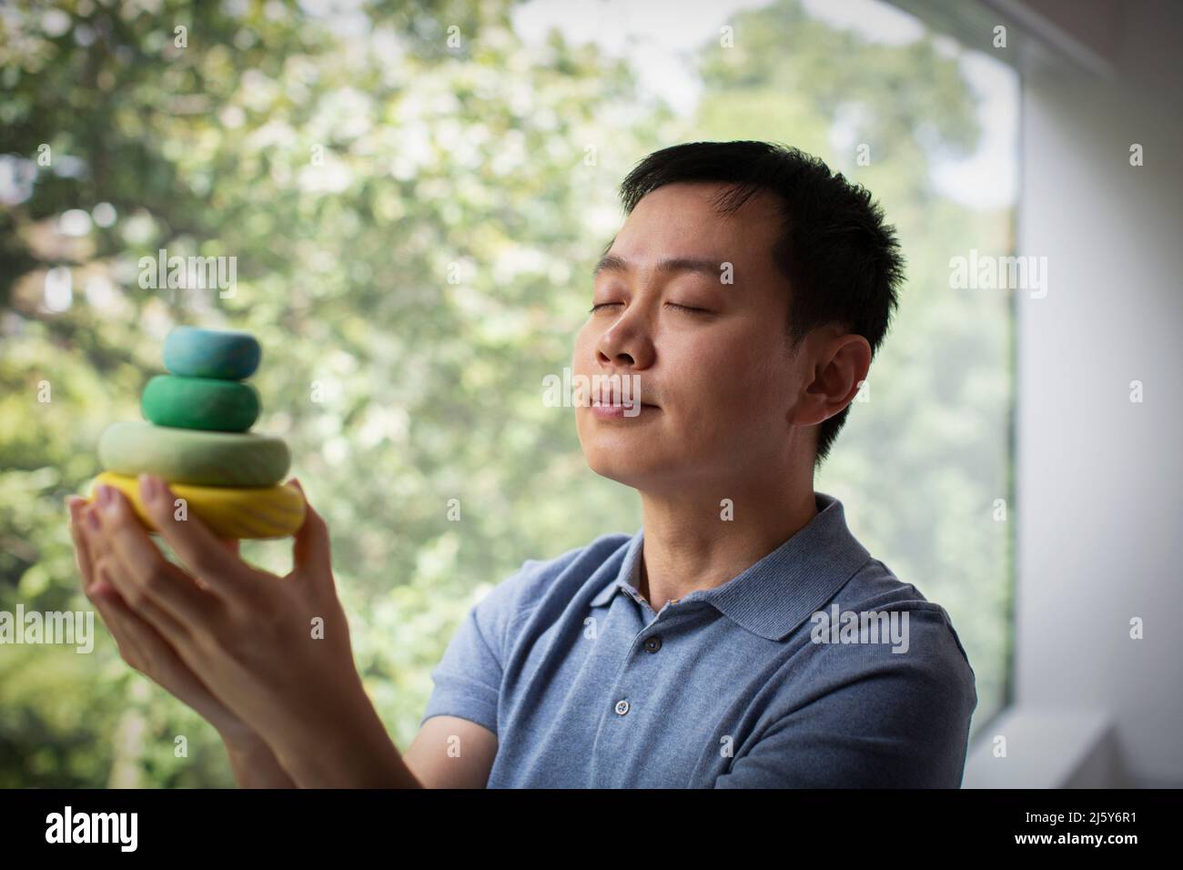 Serene man holding stacked wooden circles at window Stock Photo