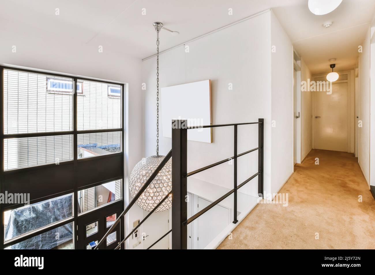 Long corridor with closed room doors and black railing of stairway in ...
