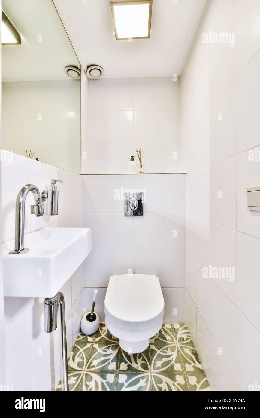 White sink at wall with mirror in light bathroom with ceramic toilet