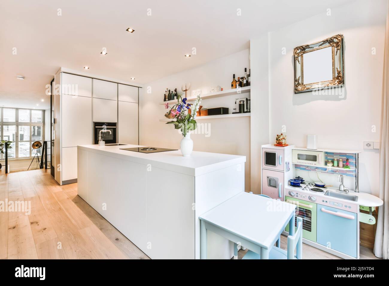 Kids kitchen placed at counter with cooker and bouquet of flowers near wall with various supplies on shelves in apartment Stock Photo