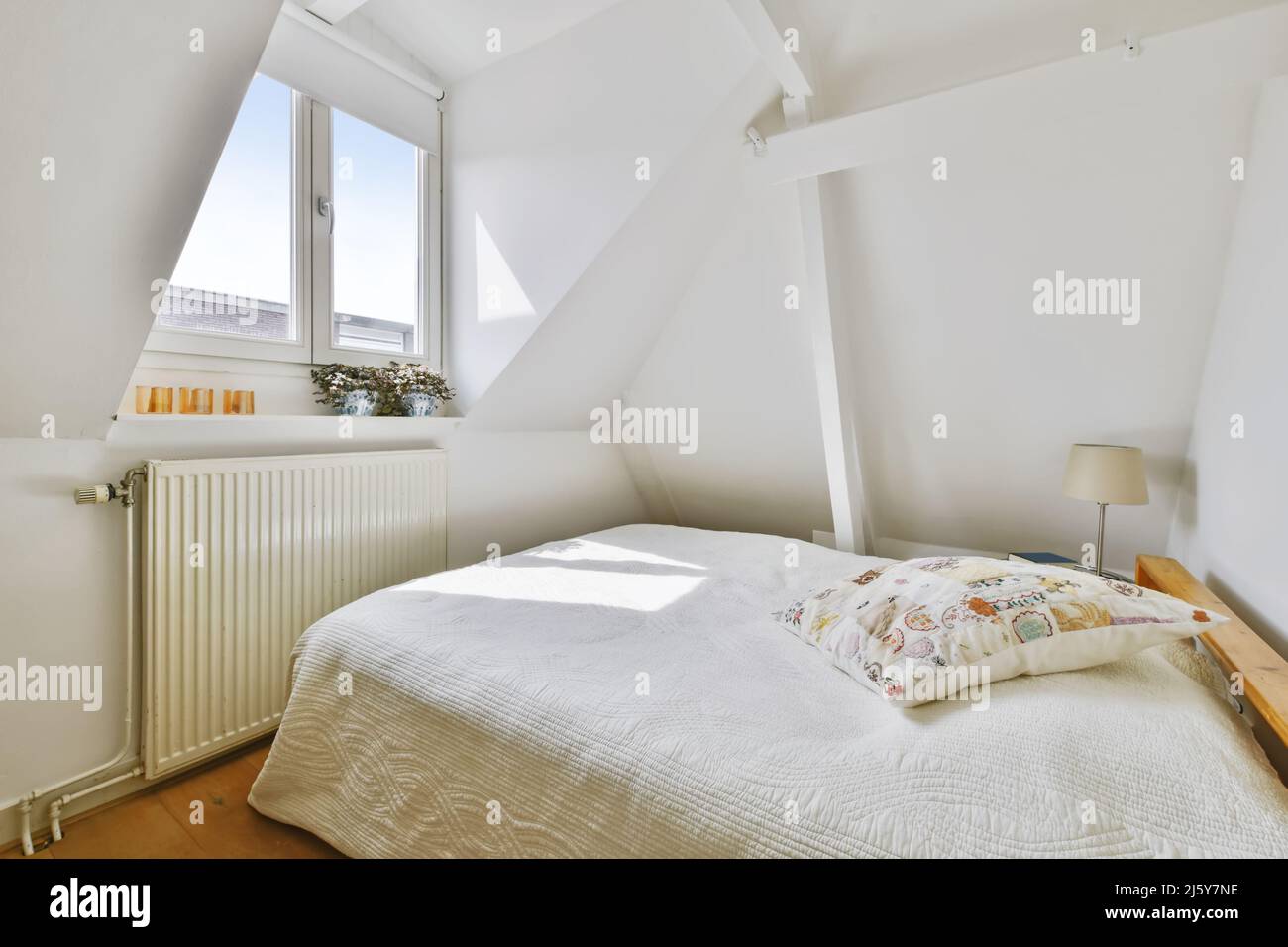 Attic room with a bed with a white quilt and cushion and in front of a ...