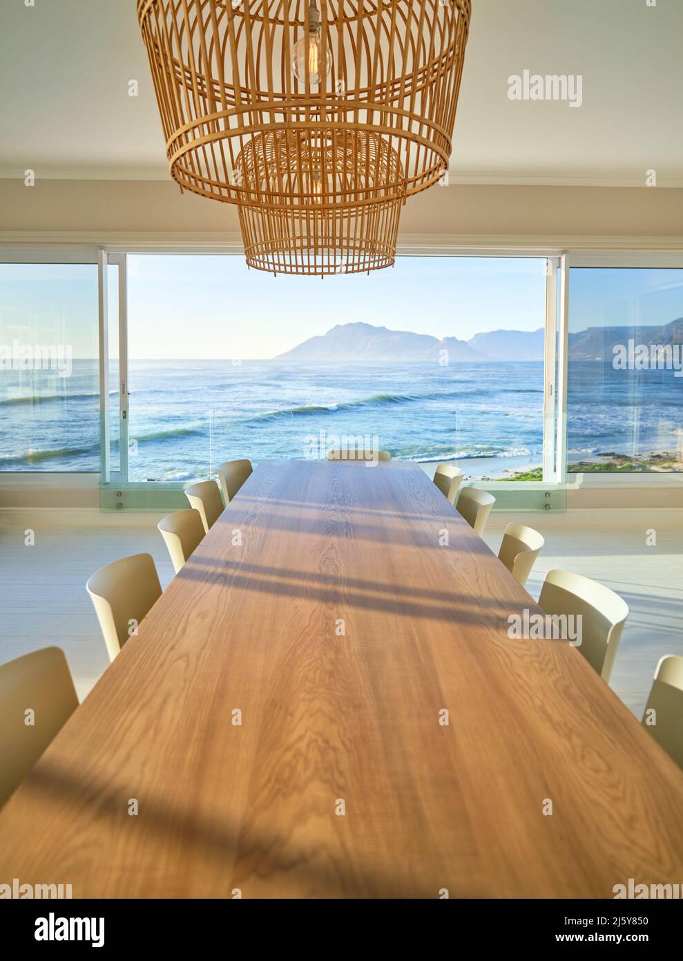 Rattan pendant lights over wooden dining table with sunny ocean view Stock Photo