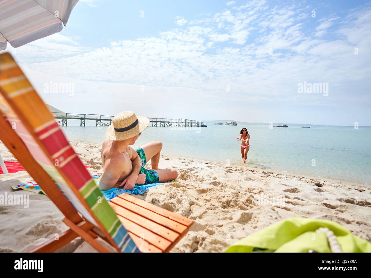 Girlfriend gesturing to boyfriend relaxing on sunny summer ocean beach Stock Photo