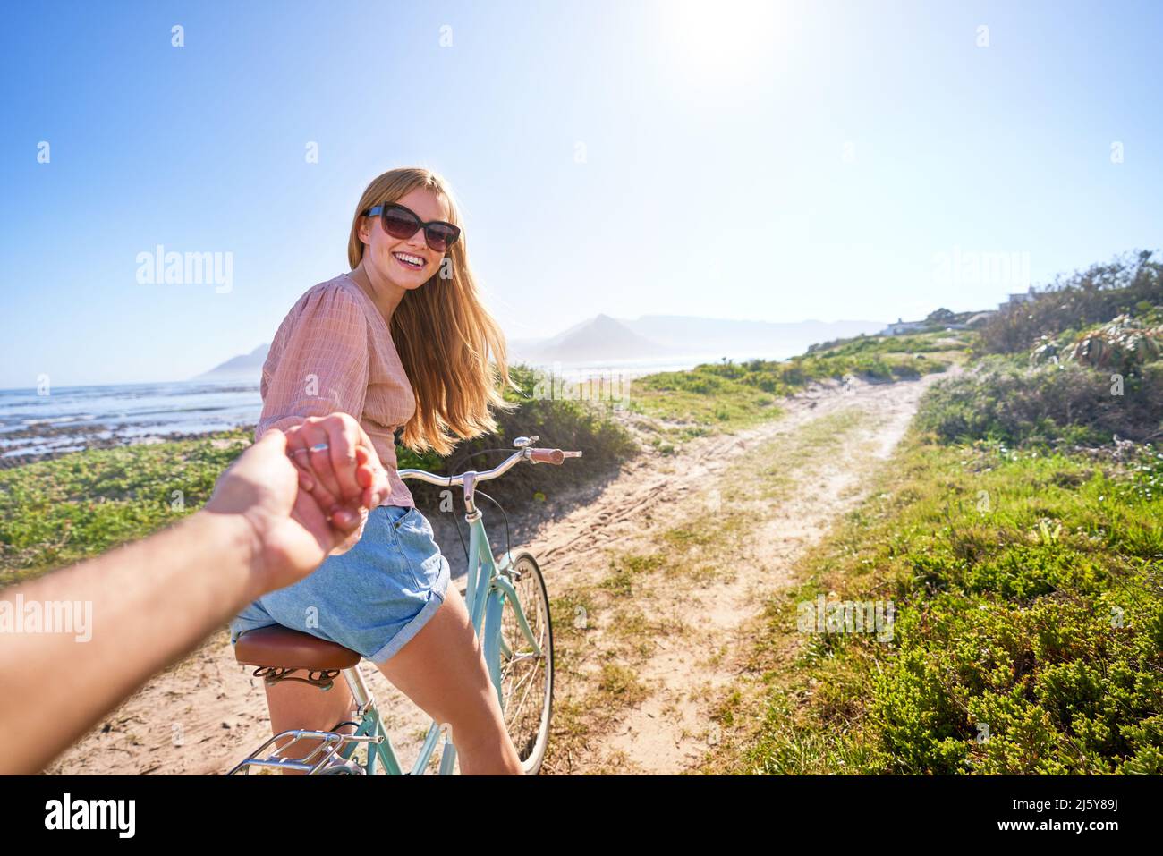 POV happy girlfriend on bicycle on sunny summer beach path Stock Photo