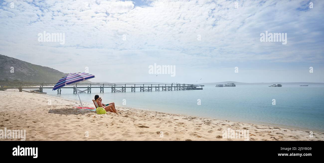 Couple sitting and relaxing on sunny, sandy ocean beach Stock Photo