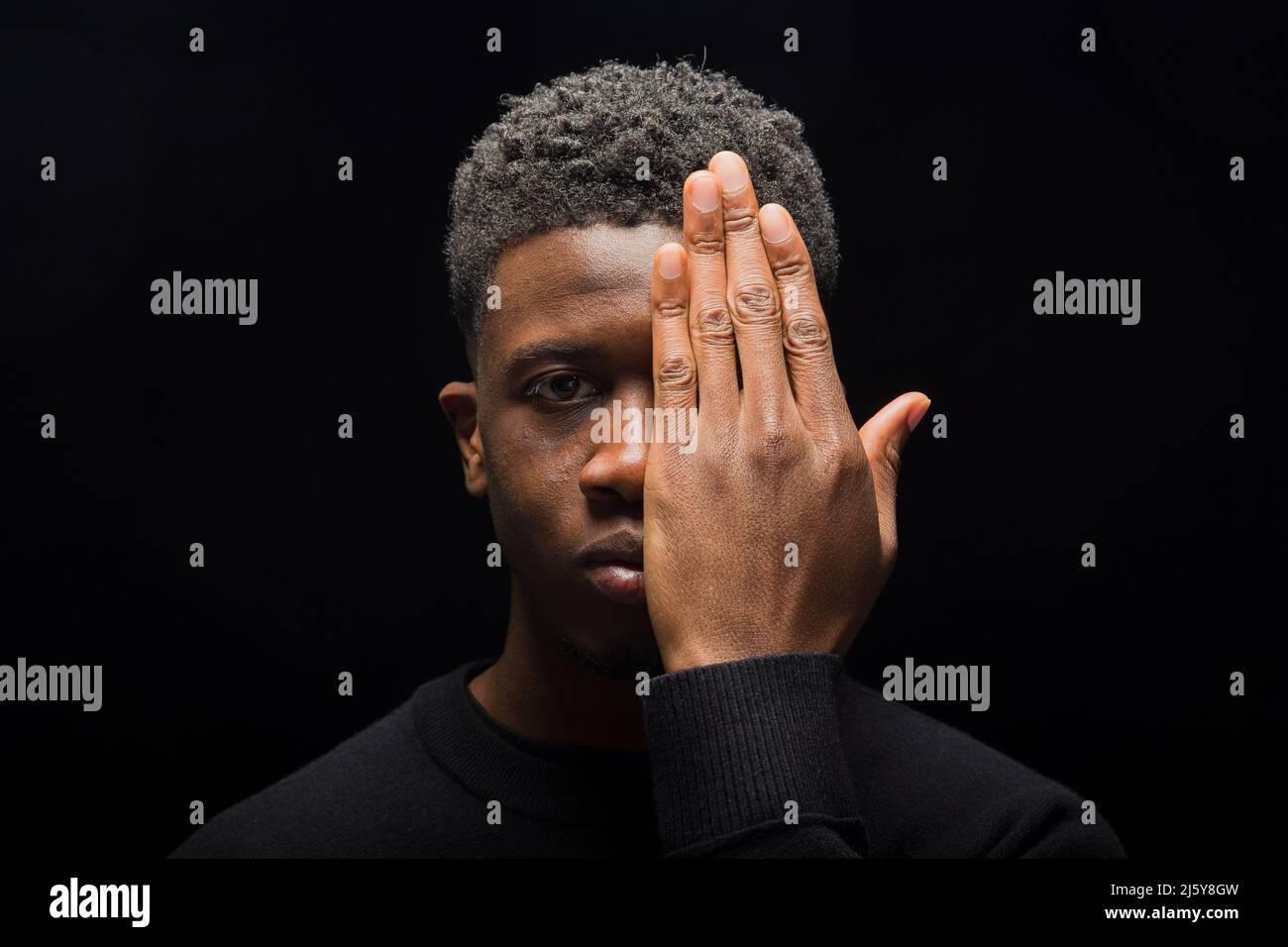 Black man with short curly hair covering half of the face with hands on ...