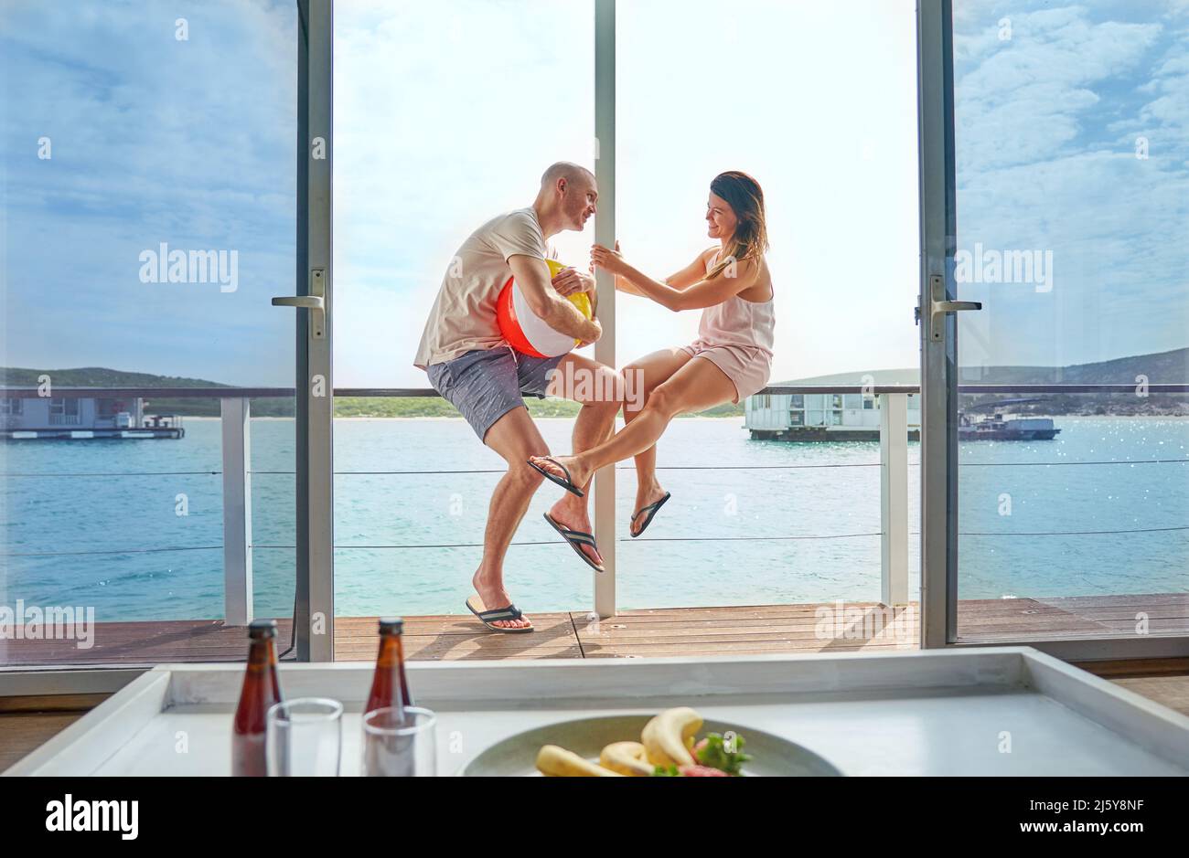Happy couple with beach ball on sunny houseboat patio Stock Photo