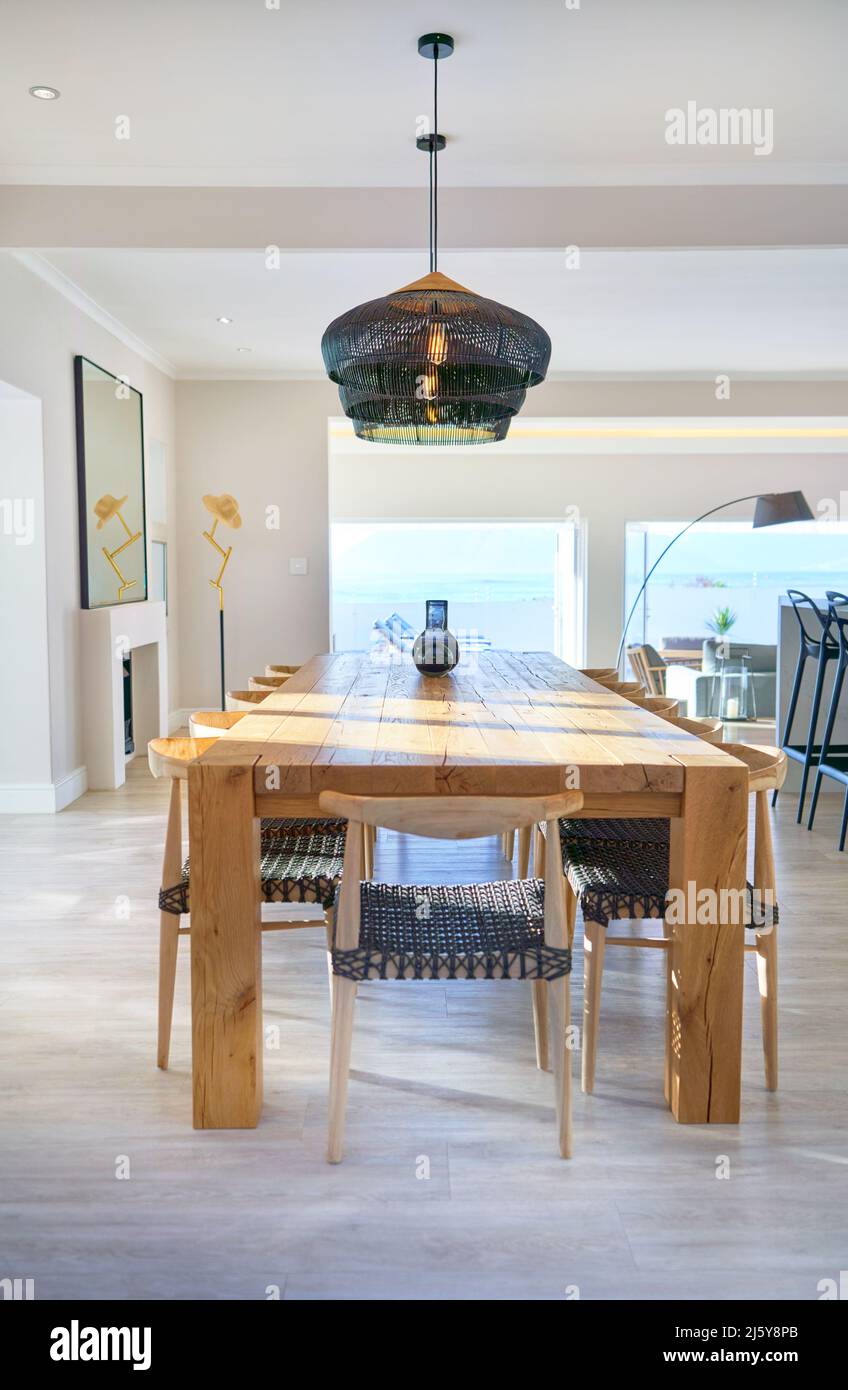 Black pendant lights over long wooden dining table in luxury home Stock