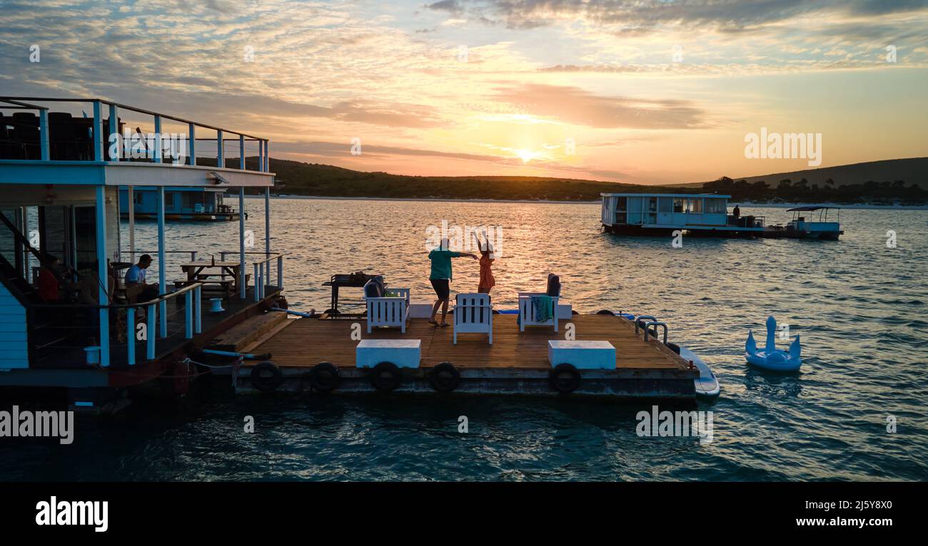 Carefree couple dancing on houseboat patio on lake at sunset Stock Photo