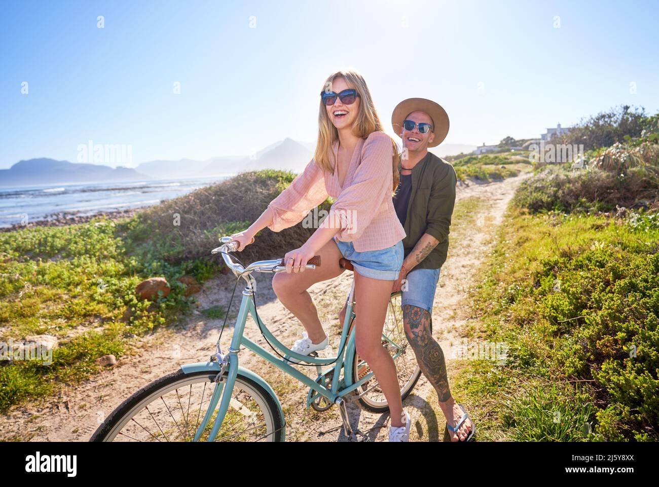 Portrait happy, carefree couple riding bicycle on sunny beach path Stock Photo