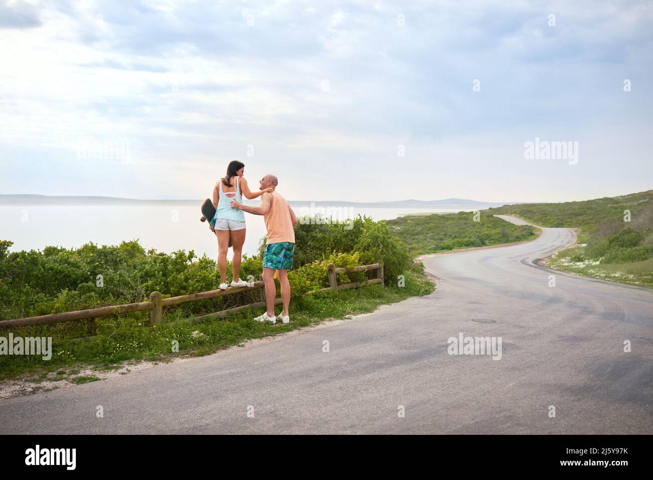 Couple standing on fence at ocean roadside Stock Photo