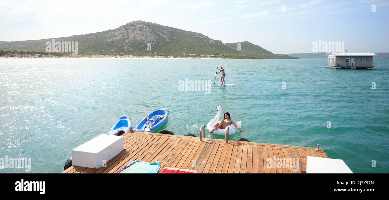 Couple paddleboarding and floating on inflatable raft on sunny lake Stock Photo