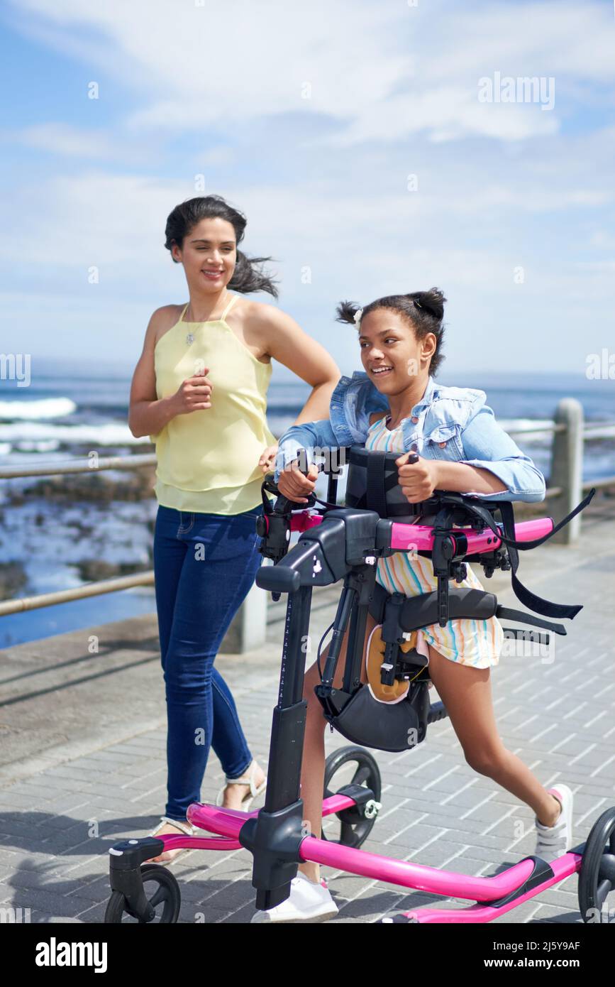 Mother and disabled daughter with rollator walking on sunny boardwalk Stock Photo