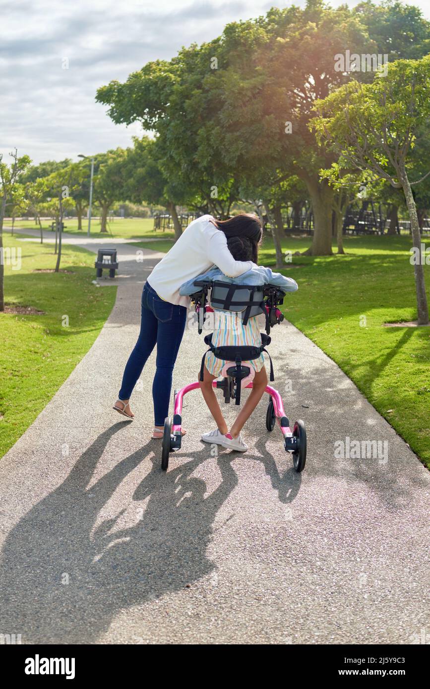 Affectionate mother hugging daughter in rollator at sunny park Stock Photo