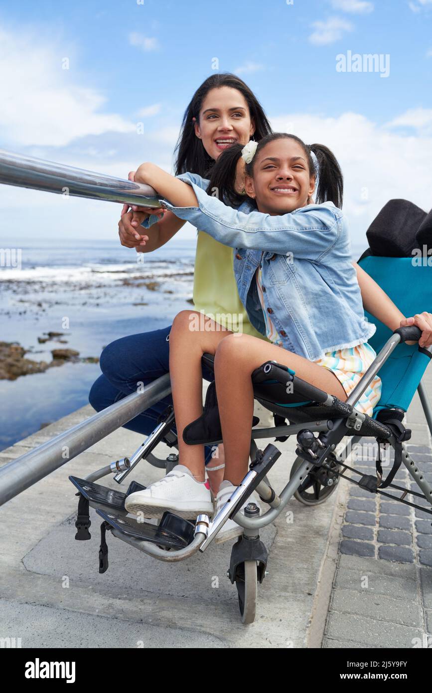 Smiling mother and disabled daughter in pushchair at beach railing Stock Photo
