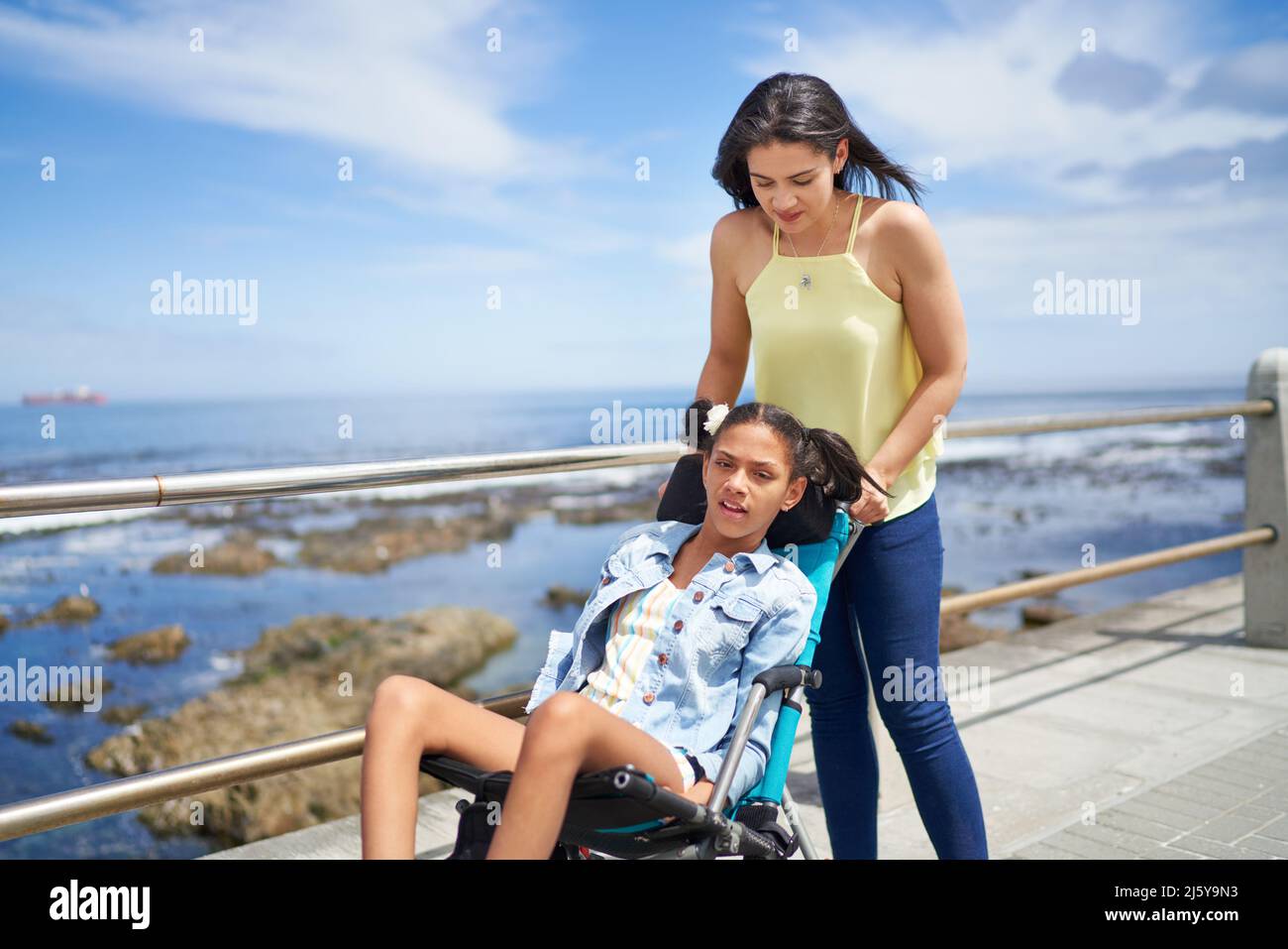 Mother pushing disabled daughter in pushchair on ocean boardwalk Stock Photo