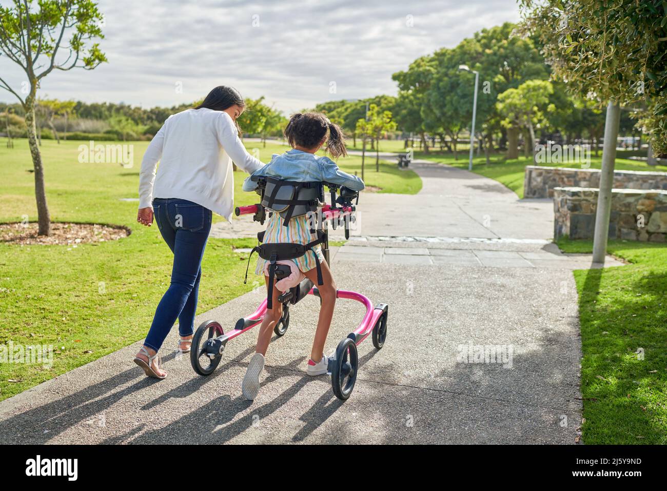 Mother and disabled daughter with rollator walking in sunny park Stock Photo