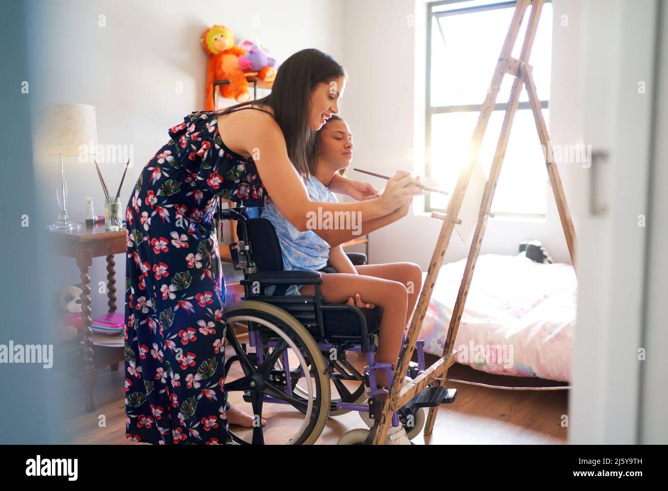 Mother and disabled daughter in wheelchair painting in bedroom Stock Photo