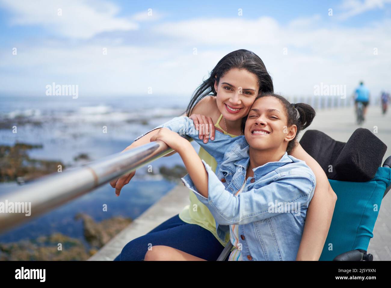 Portrait happy mother and disabled daughter at ocean railing Stock Photo