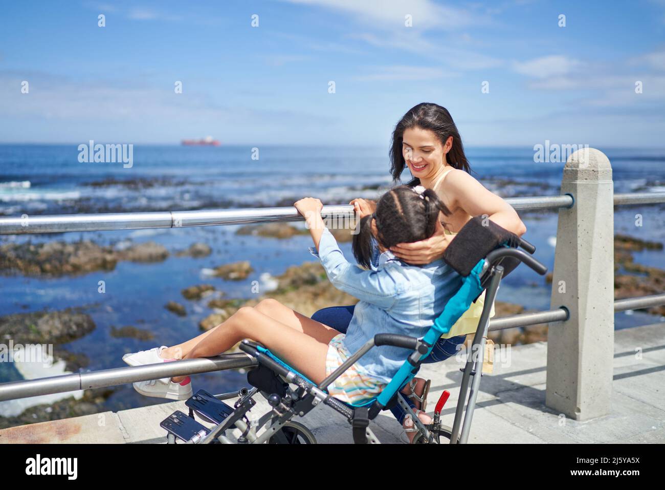 Mother and disabled daughter in pushchair on sunny ocean boardwalk Stock Photo