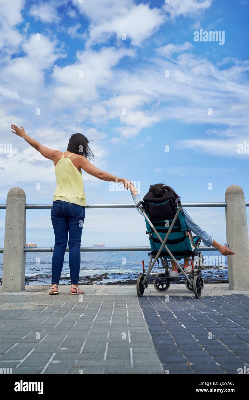 Mother and disabled daughter with arms outstretched on beach boardwalk Stock Photo