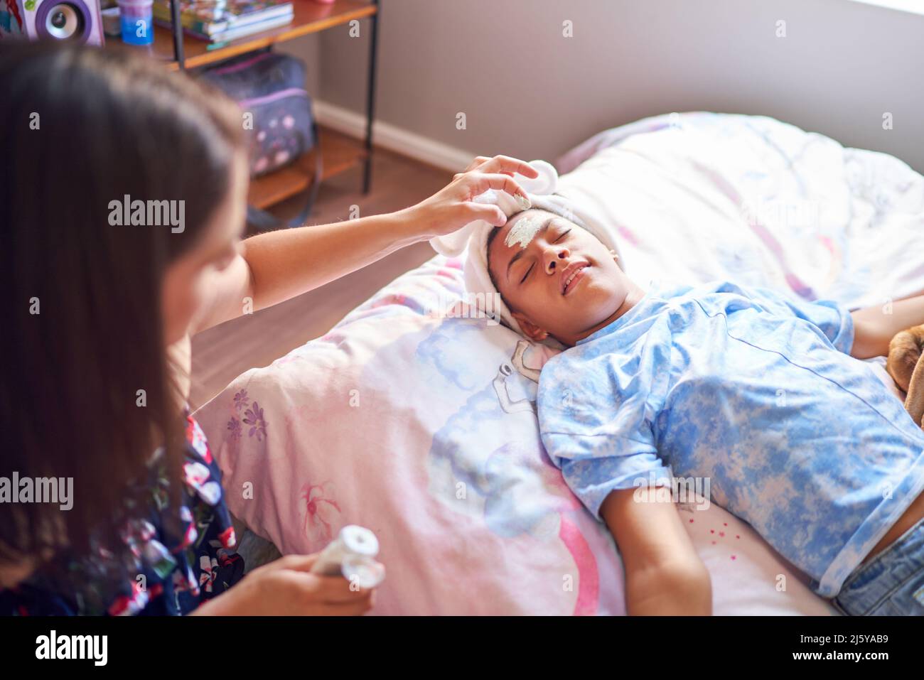 Mother giving disabled daughter a facial on bed at home Stock Photo