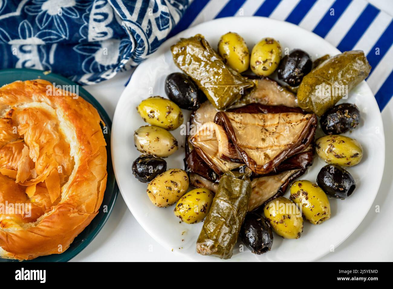 Greek appetizer plate with olive, sliced eggplant and dolmades (vine leaf stuffed with rice), pastry tyropita with cheese, closeup. Stock Photo