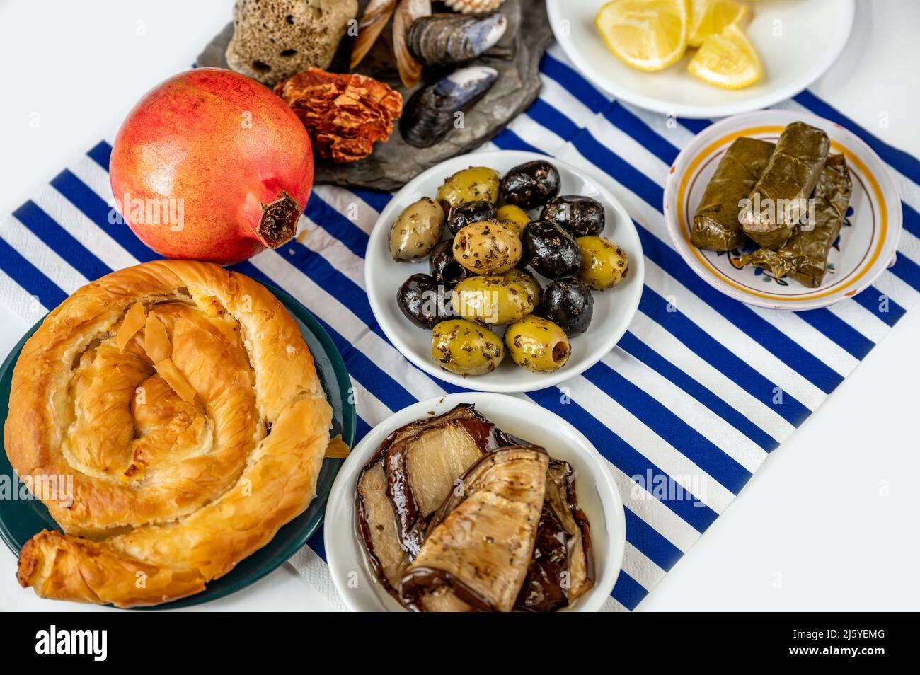 Table full of traditional greek specialty food. Pickled slices eggplant, dolmades (stuffed wine leaf with rice), olive, spiral pastry with cheese (tyr Stock Photo