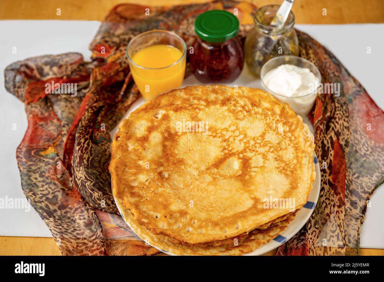 Pancake, orange juice, raspberry jam and yoghurt, red scarf on table