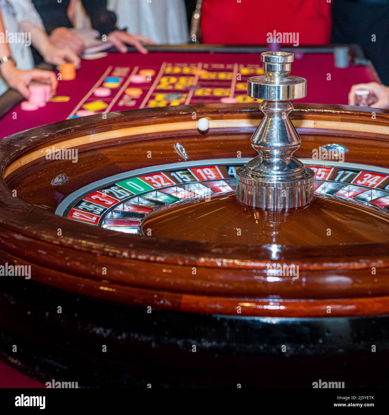 Roulette wheel with red casino table in the distance. Stock Photo