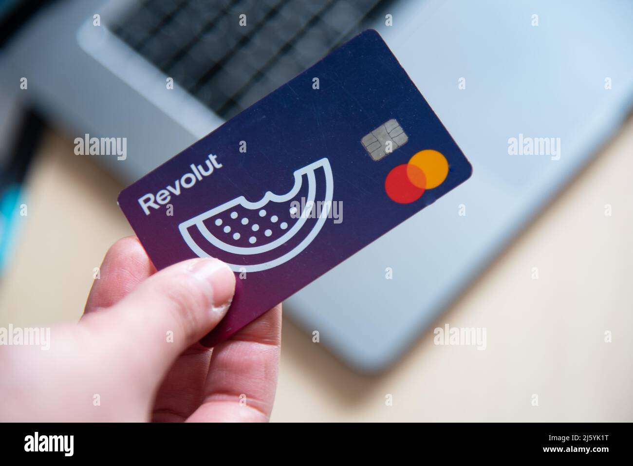 Human hand holding a revolut debit card. Mobile phone app digital payments online with laptop computer Stock Photo