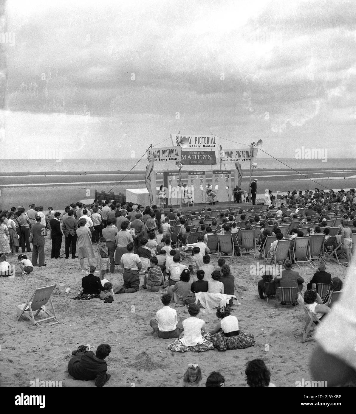 1957, people gather on the beach at Prestatyn, North Wales to watch a Sunday Pictorial Beach Beauty Contest. The newspaper had organised a 'You May Be The MARILYN of Prestatyn Sands Competition, to find a female whose figure matched that of Marilyn Monroe. In the 1950s and early 60s, the American actress had become not just a hollywood superstar but an international one. On the stage, three cut-outs, 1) How Do You Shape, B) Does Your Figure Fit? C) Are You A Marilyn? The Pictorial, as the newspaper was known, spend the summer of this year touring Britain's seaside resorts to find its Marilyn. Stock Photo