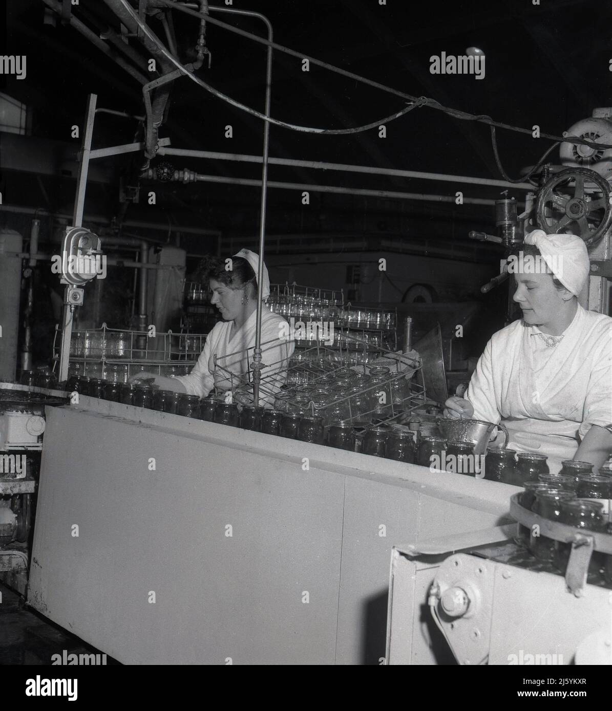 1960s, historical, two female factory workers sitting at a production line  at a food company, filling up the glasss jars with a fruit preserve, most  probably marmalade, Oxford, England UK Stock Photo -