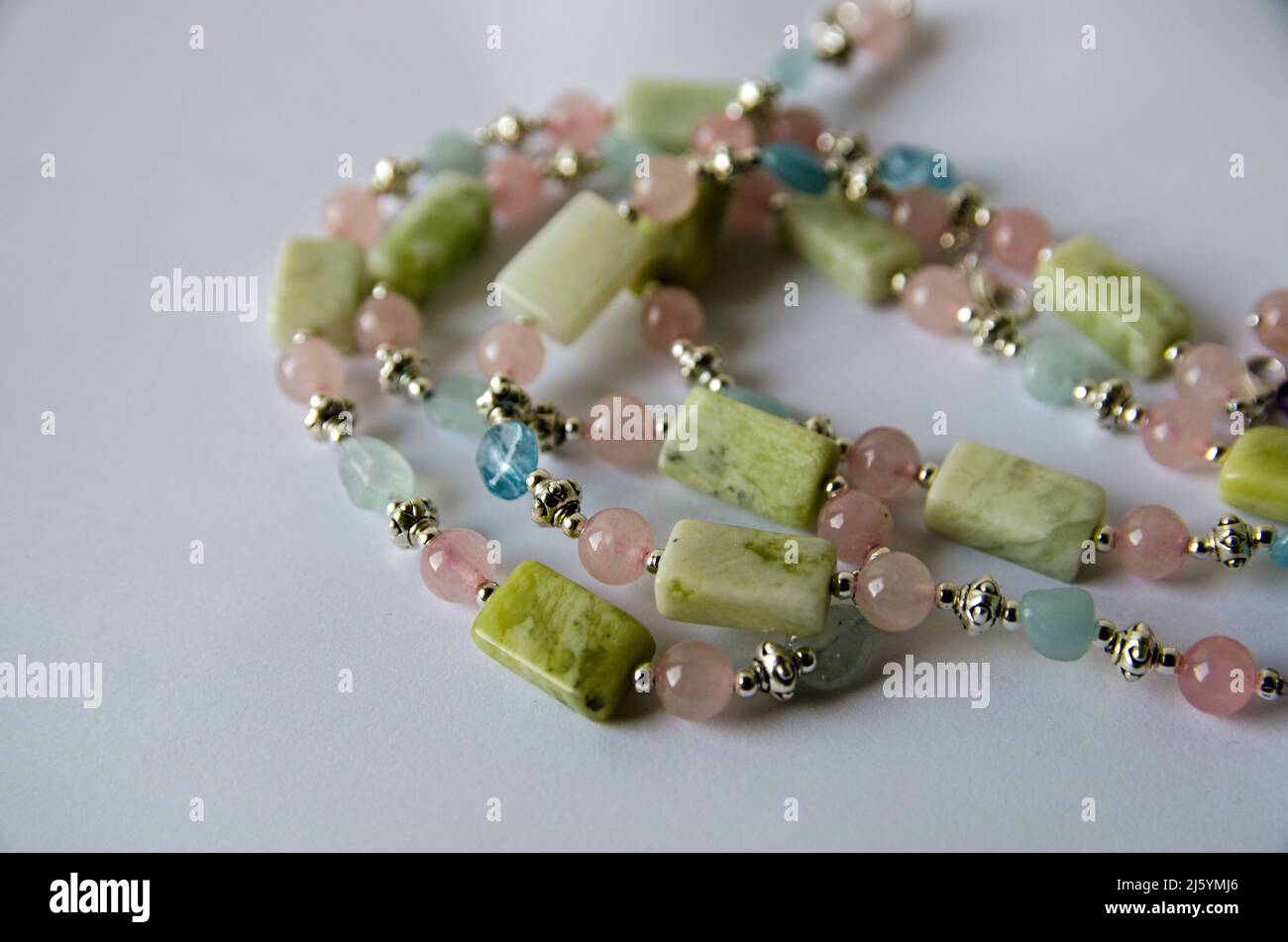 A handmade necklace crafted from pastel coloured beads made from aquamarine, rose quartz and jade.  Viewed on a white background with drop shadow. Stock Photo