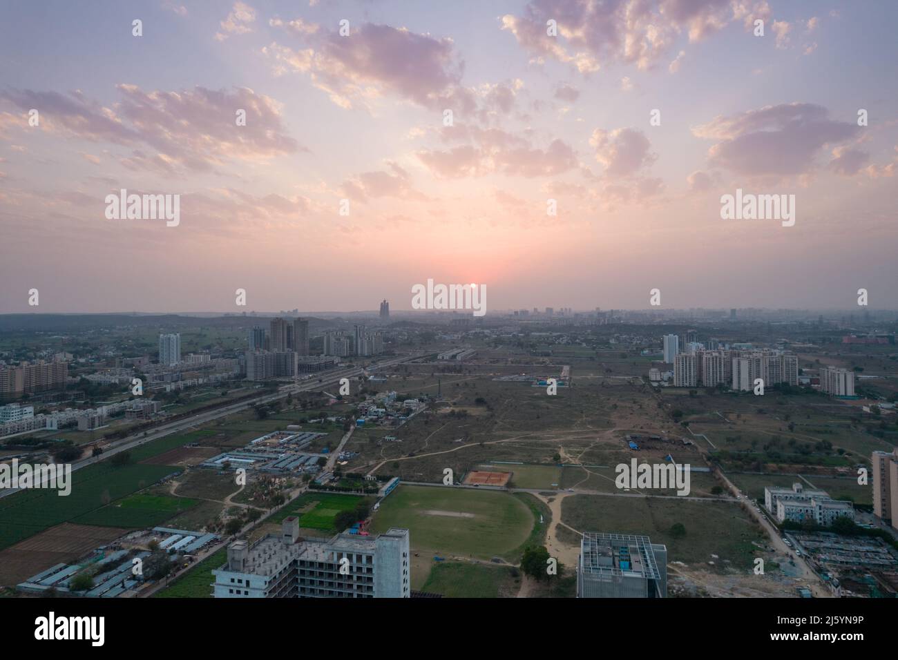 aerial drone shot passing over a building with homes, offices, shopping centers moving towards skyscapers in front of sunset showing the empty Stock Photo