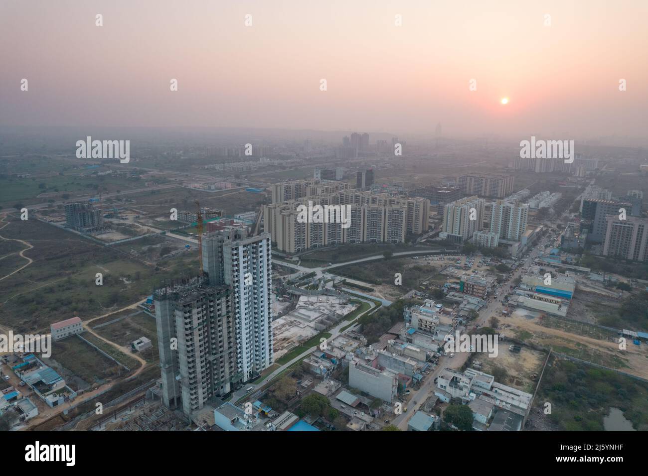 aerial drone shot passing over a building with homes, offices, shopping centers moving towards skyscapers in front of sunset showing the empty Stock Photo