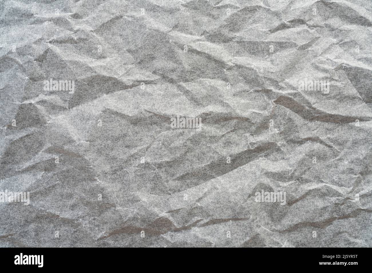 the reflections of light on a sheet of crumpled paper on a grey surface ...