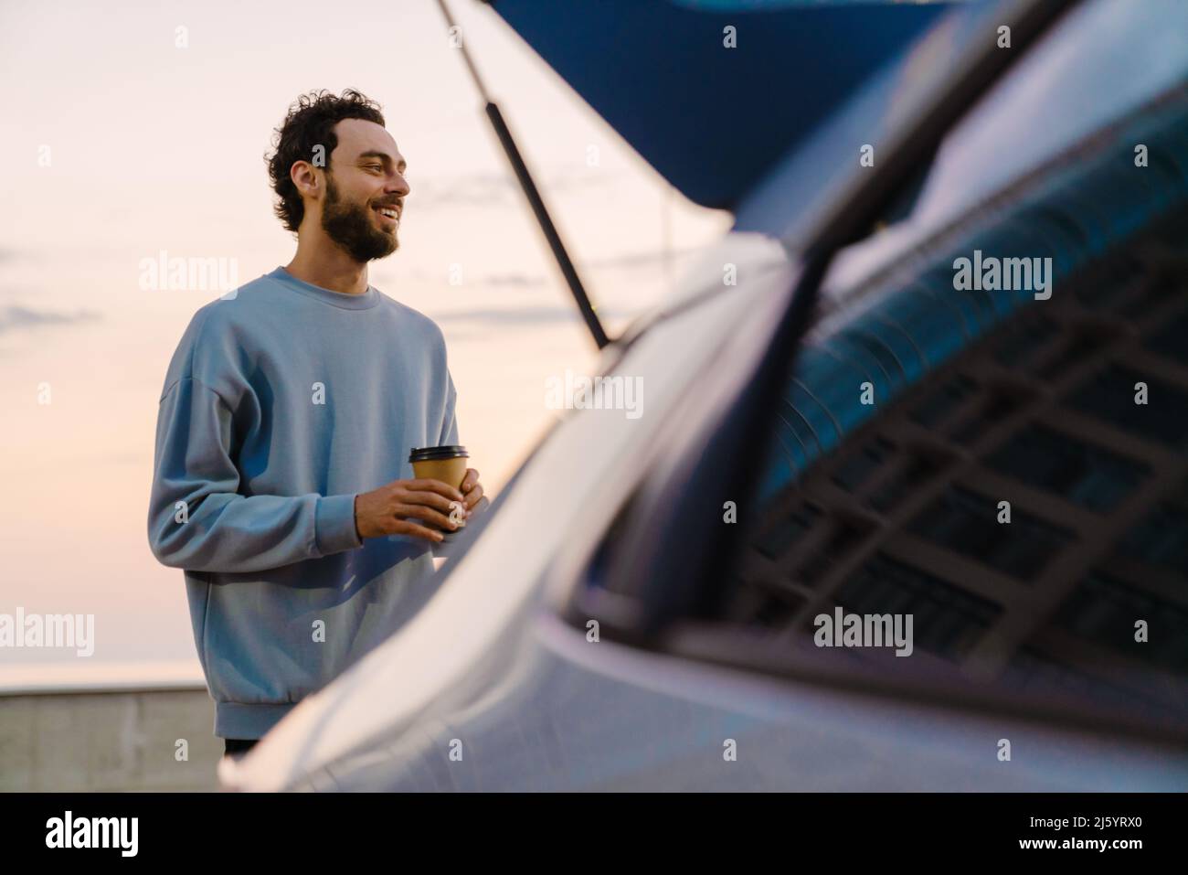 Young man smiling while drinking coffee on parking outdoors Stock Photo