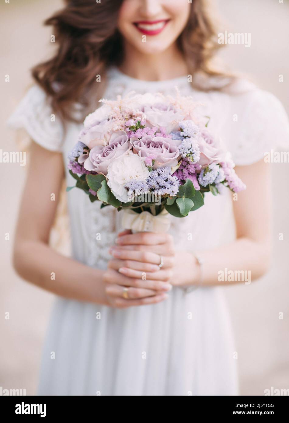 Wedding bouquet in white and violet colours, close up. Modest beautiful smiling bride with round purple wedding bouquet. White lace and silk wedding d Stock Photo