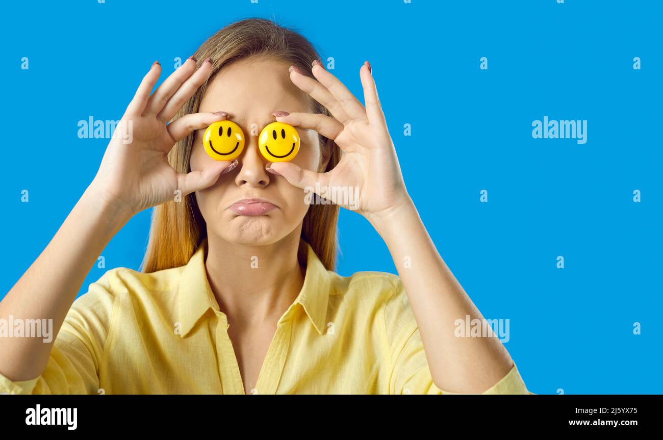 Sad woman trying to fake happiness, holding happy emojis and hiding her real emotions Stock Photo