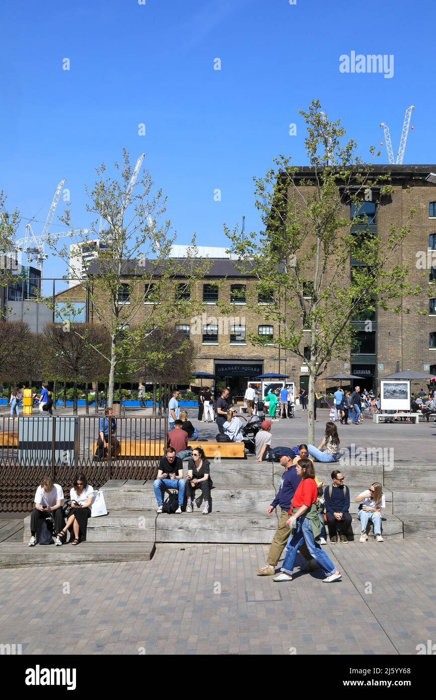 People relaxing in spring sunshine on Granary Square with St Martins Central School of Art behind, at Kings Cross, London, UK Stock Photo