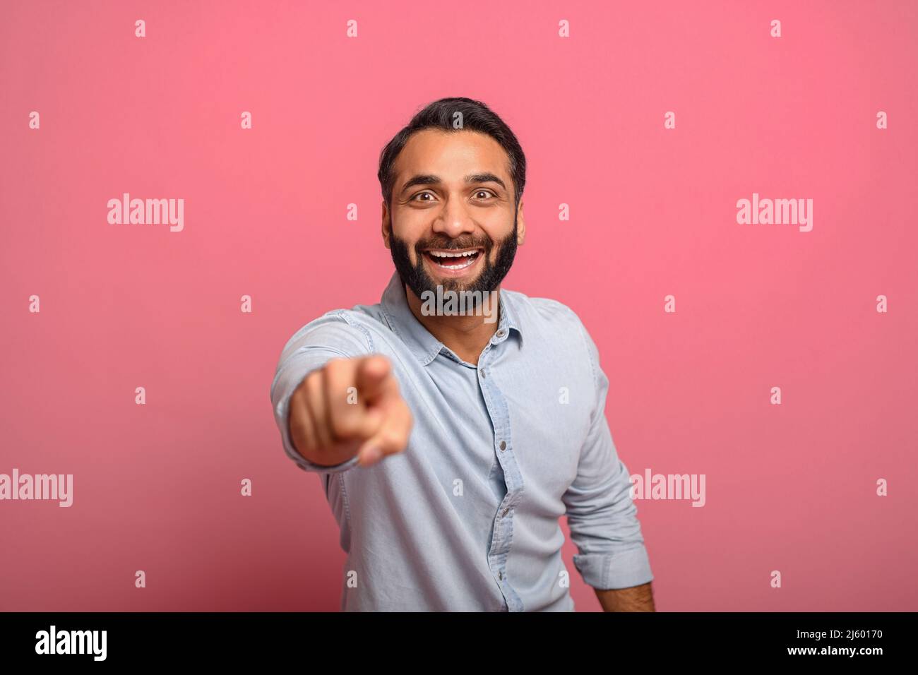 Joyful excited Indian middle-aged man in jeans shirt points fingers at the camera, surprised handsome multiracial guy choosing you, selecting viewer isolated on pink, laughs at you Stock Photo