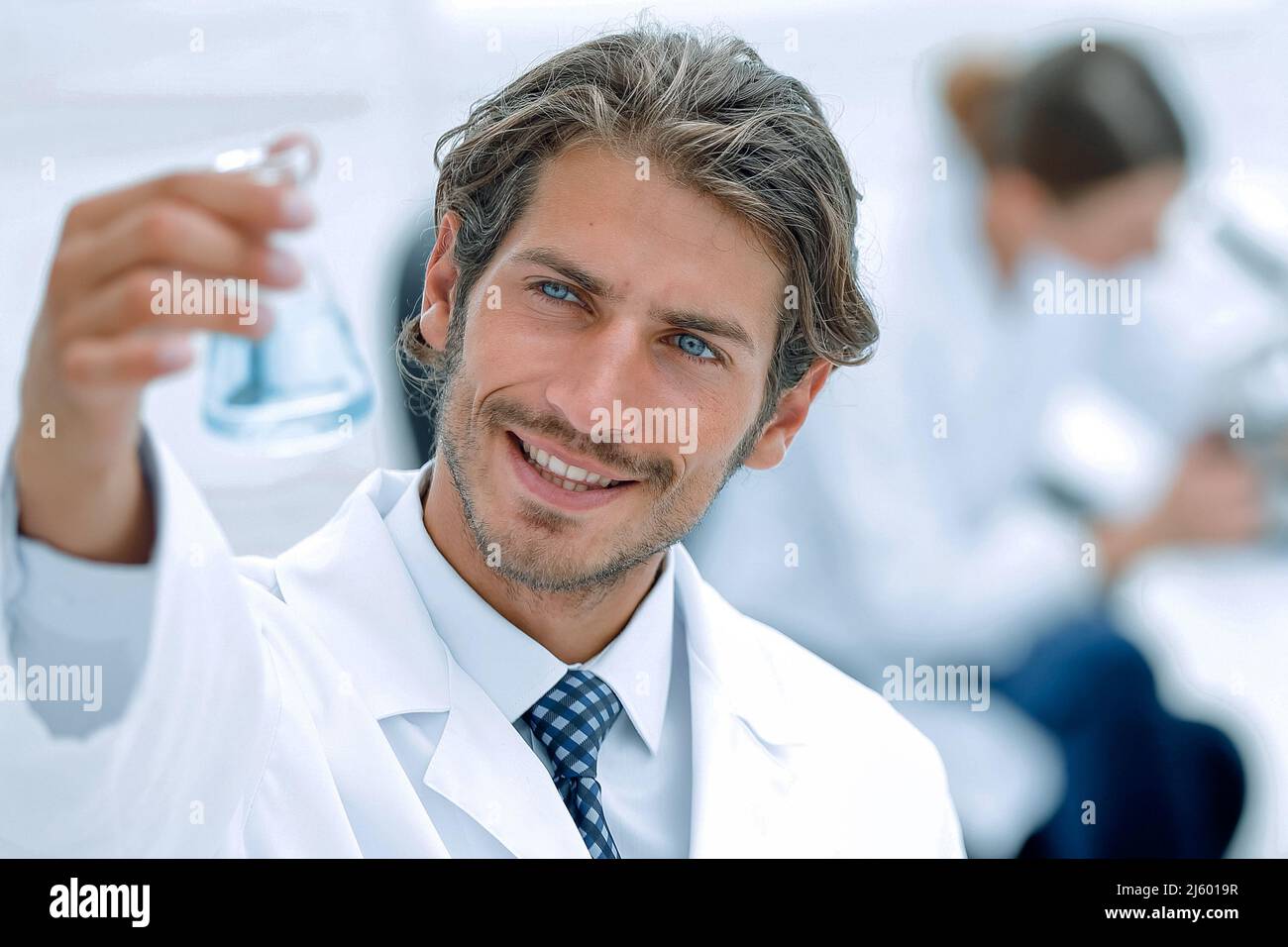 Concentrated male laboratory scientist holding flask with blue liquid ...