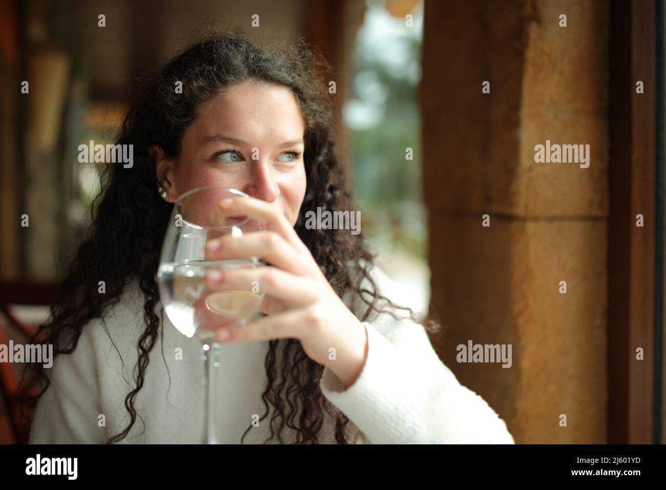 Happy woman holding glass of water looks through window in a restaurant interior Stock Photo