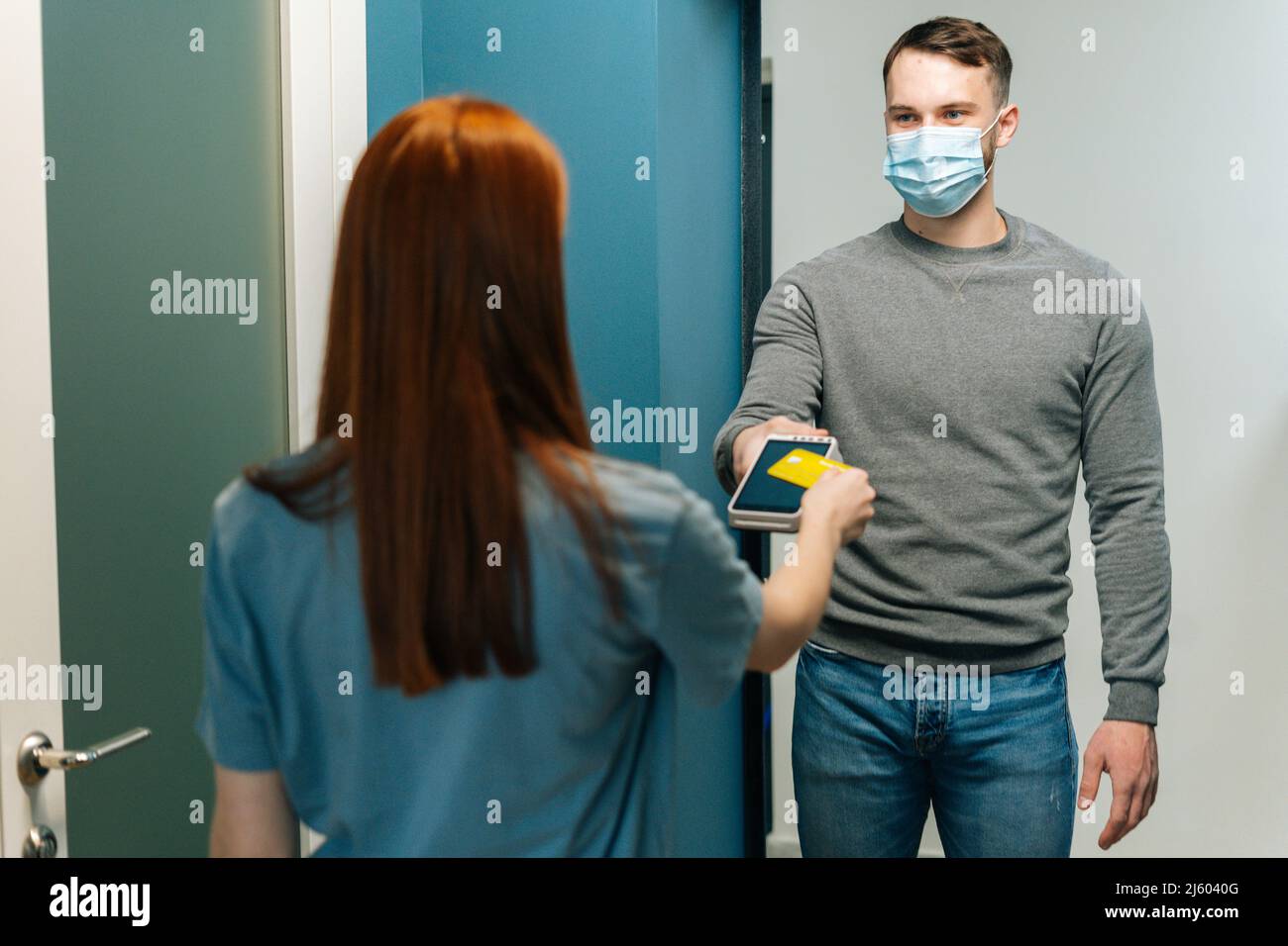 Handsome courier male wearing protective face mask giving POS wireless terminal to making contactless payment via credit card Stock Photo