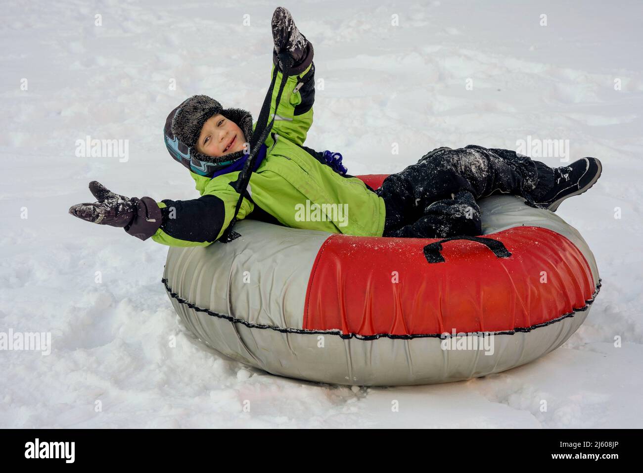 Funny Caucasian boy 5 years old rides in winter on a big inflatable cheesecake Stock Photo