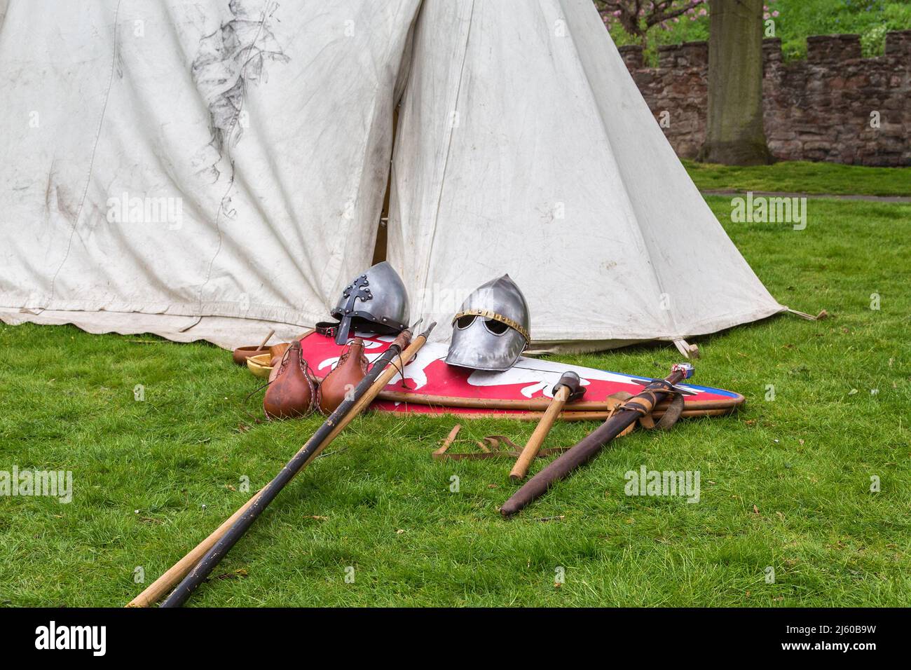 The helmets, shields and weaponry of medieval knights laid out on the grass by a tent. Part of an historical society living history camp. Stock Photo