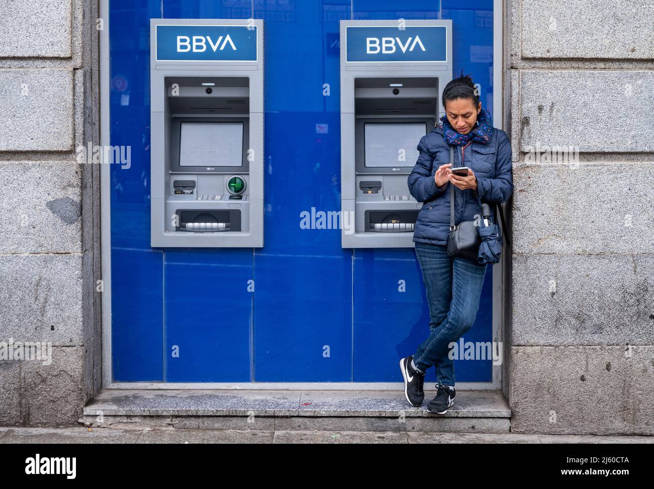 Madrid, Spain. 26th Apr, 2022. A woman uses her smartphone next to an ATM machine at the Spanish multinational BBVA bank branch in Spain. Pedestrians walk past the Spanish multinational Banco Bilbao Vizcaya Argentaria SA (BBVA) bank in Spain. (Photo by Xavi Lopez/SOPA Images/Sipa USA) Credit: Sipa USA/Alamy Live News Stock Photo