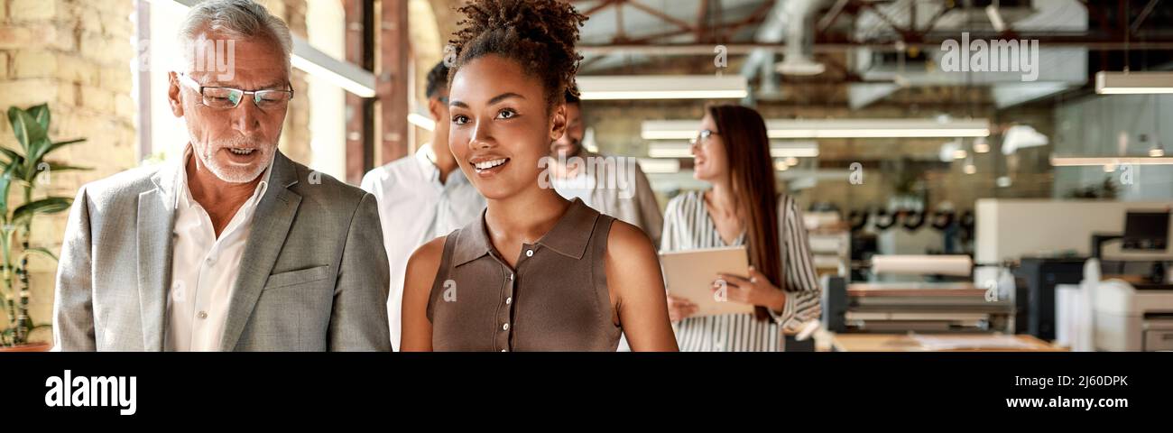 Sharing ideas. Two business experts discussing something while walking with colleagues through the office corrido Stock Photo
